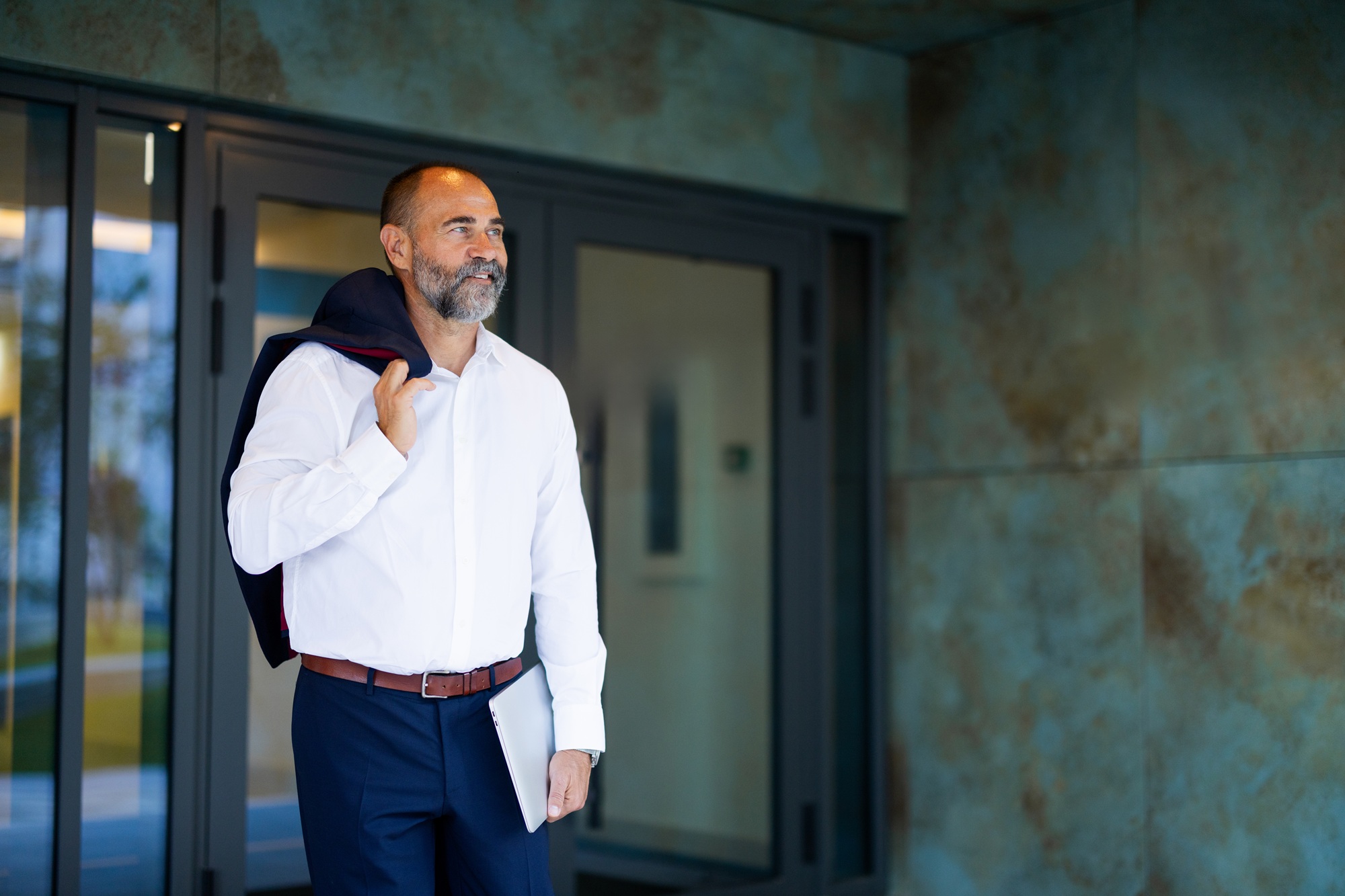 Portrait of a successful businessman holding his jacket and a tablet, looking away