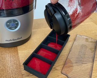 Decanting fresh raspberry juice made in Nutribullet Pro into black ice cube mold