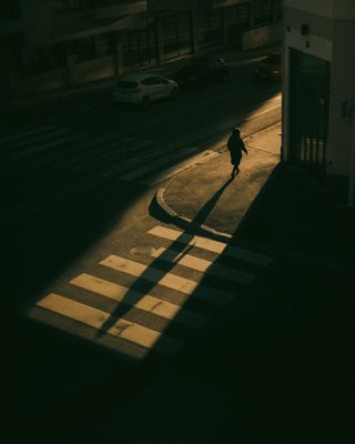 golden sunlight spilling over a crosswalk with someone about to cross casting a long shadow over the road