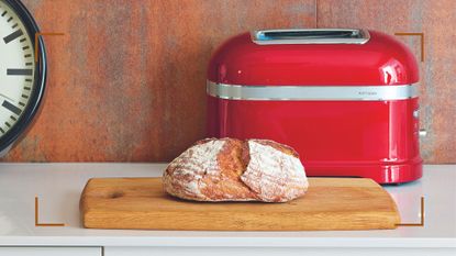 Red toaster in a contemporary wooden kitchen with a fresh loaf of bread to show why how to clean a toaster is an essential chore