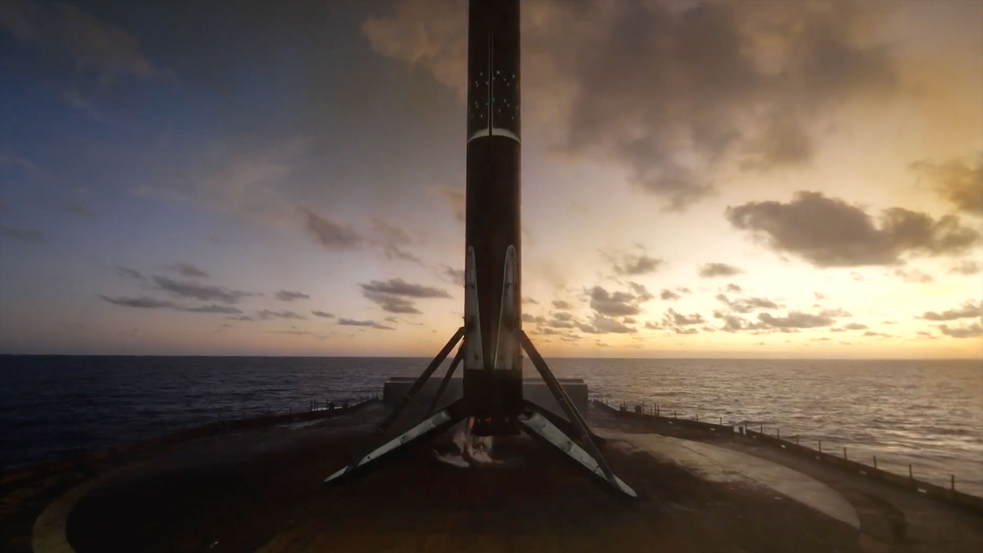 the first stage of a rocket stands atop an ocean-based platform at sunset