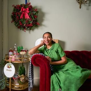 Lady sitting on red velvet sofa, with christmas decorations on wall and table