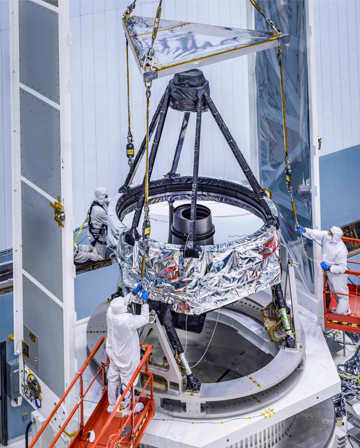 Technicians in white stand around a large apparatus with black metal framework.