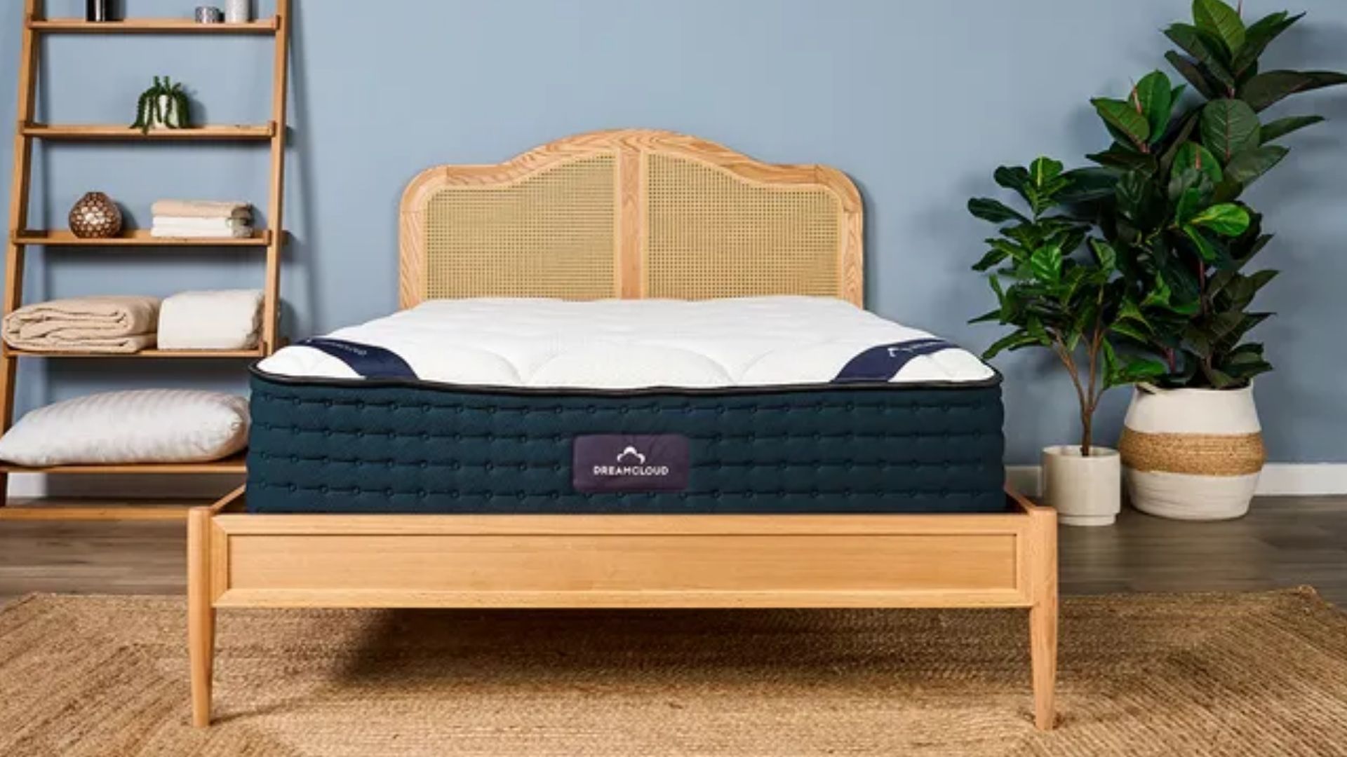 The image shows the DreamCloud Classic hybrid mattress on a wooden bed frame in a blue bedroom
