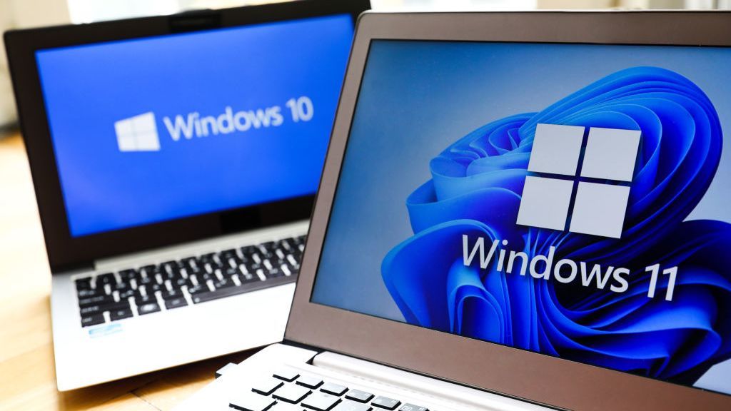 Two laptops sat one in front of the other with Windows 10 and Windows 11 logos displayed