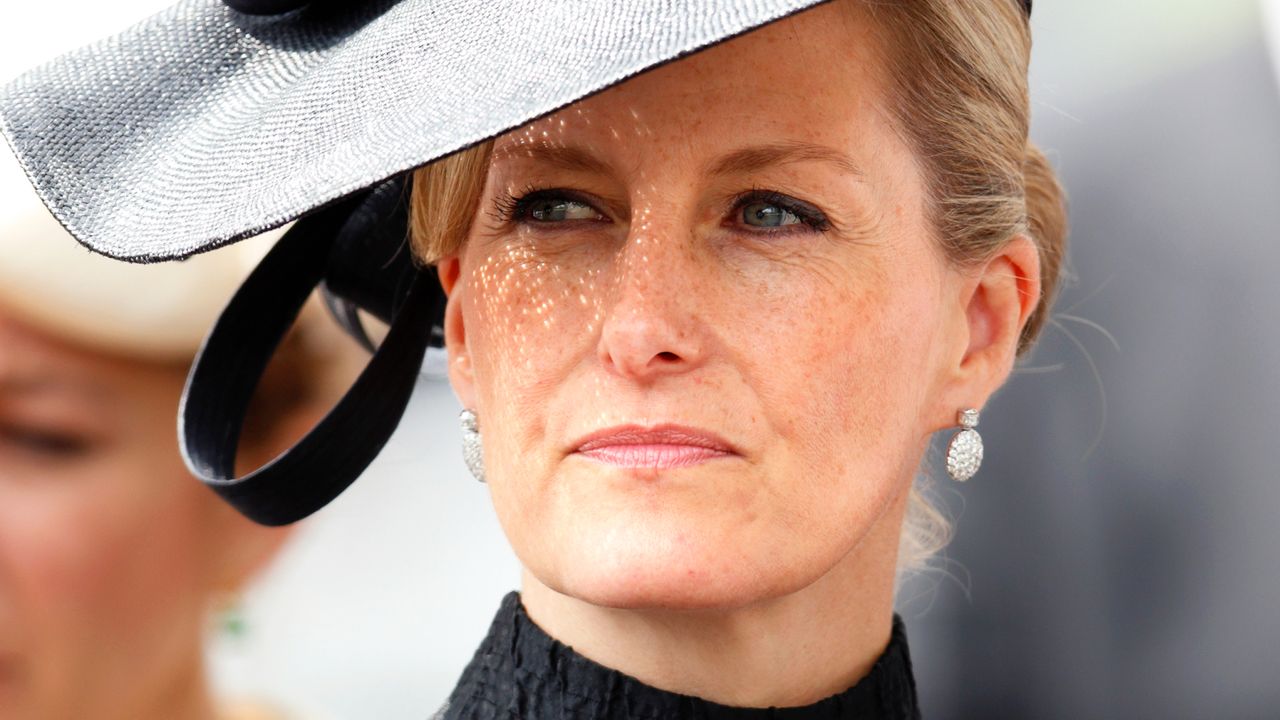 A headshot of Duchess Sophie wearing a black dress and huge black hat with diamond earrings at Royal Ascot 2014