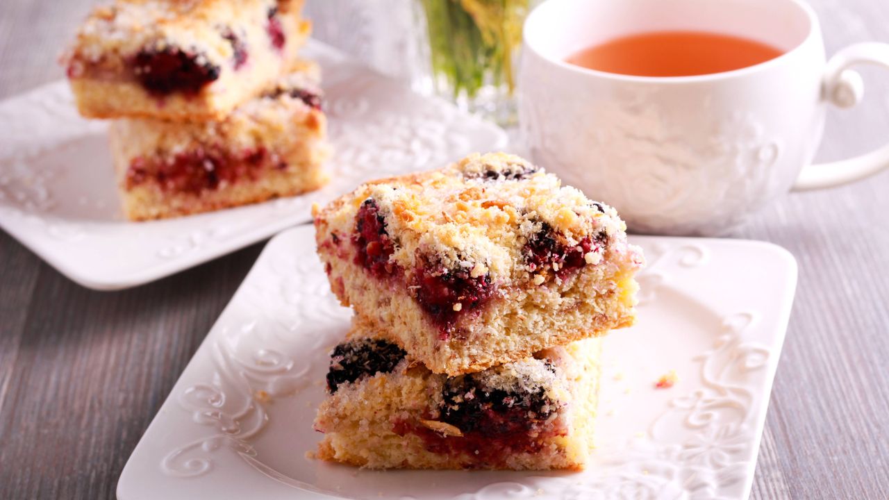 Blackberry flapjacks with apples and caramel on a small white plate with a cup of tea 