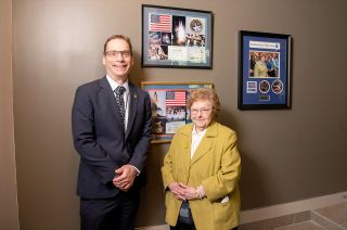Retired Senator Barbara Mikulski poses with Kenneth Sembach, director of the Space Telescope Science Institute (STScI) in front of framed space memorabilia from Mikulski's collection. 