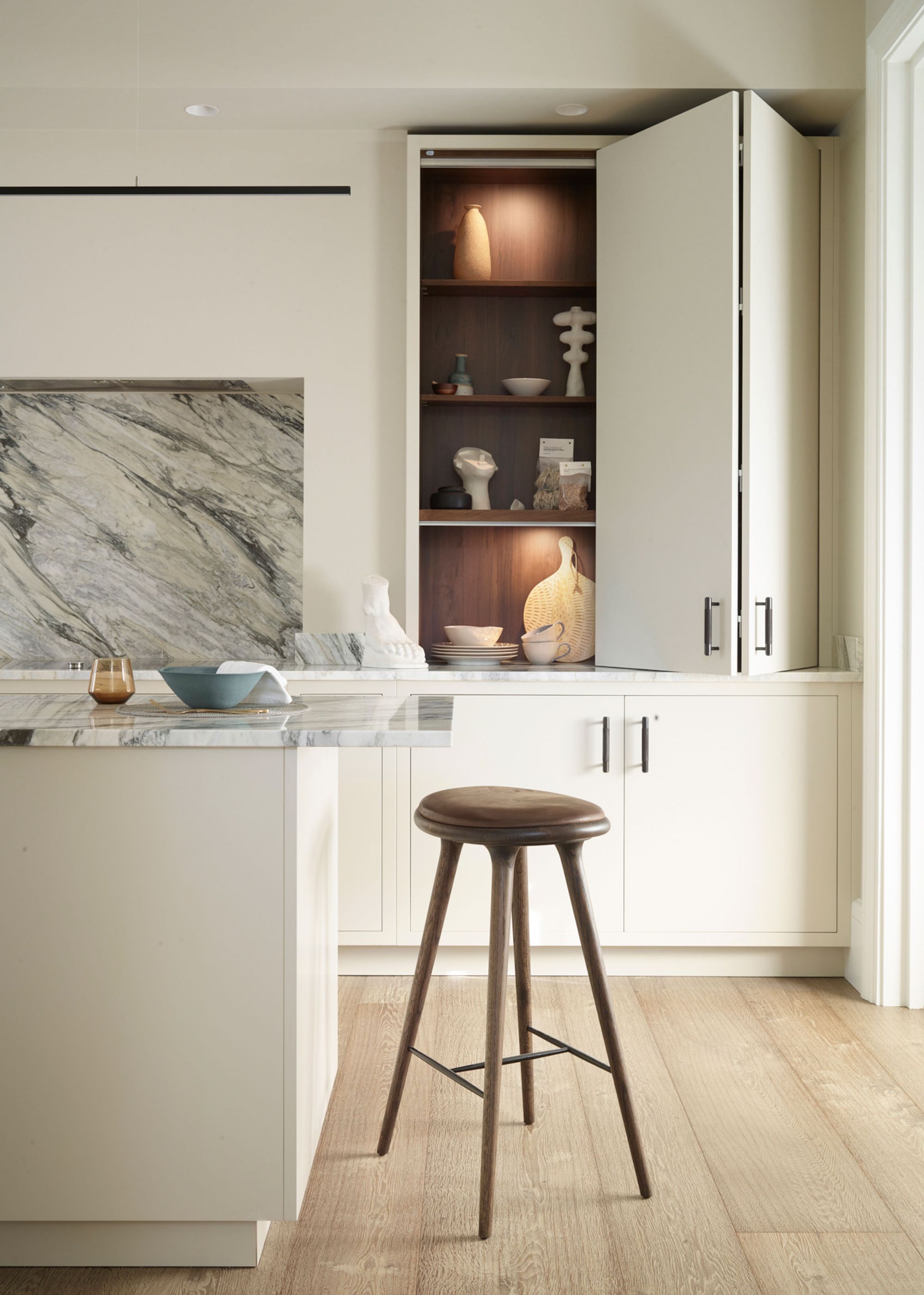 a kitchen with a bifold pantry door with lighting as well as a view of an island with a bar stool next to it