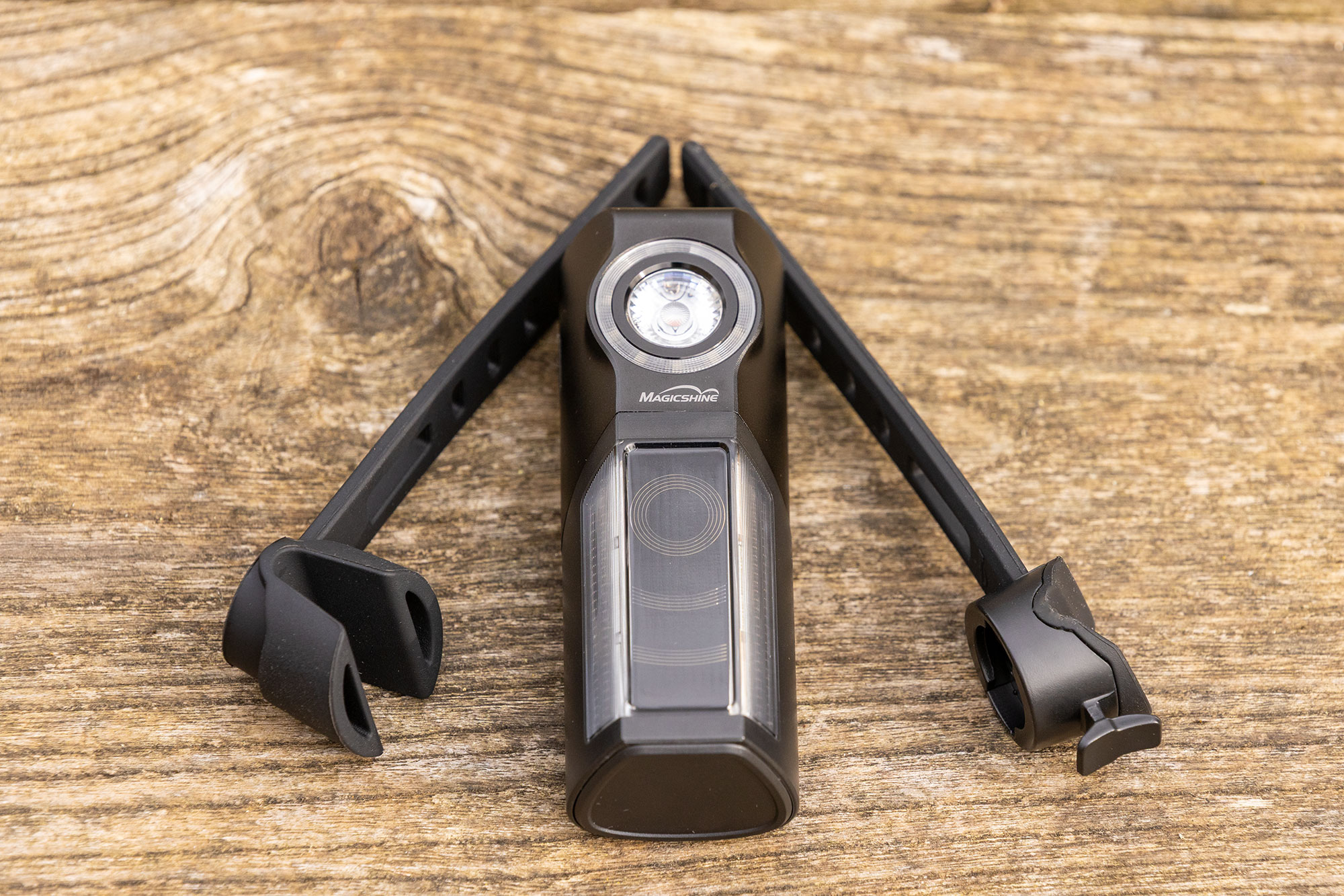 Magicshine Seemee R300 pictured off bike, on a wooden surface, complete with the two supplied straps