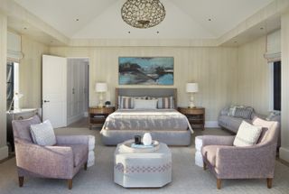 A traditional-style bedroom with two purple armchairs facing a table