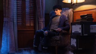 Teen sits in a chair at night with a lamp on next to him in Agatha All Along