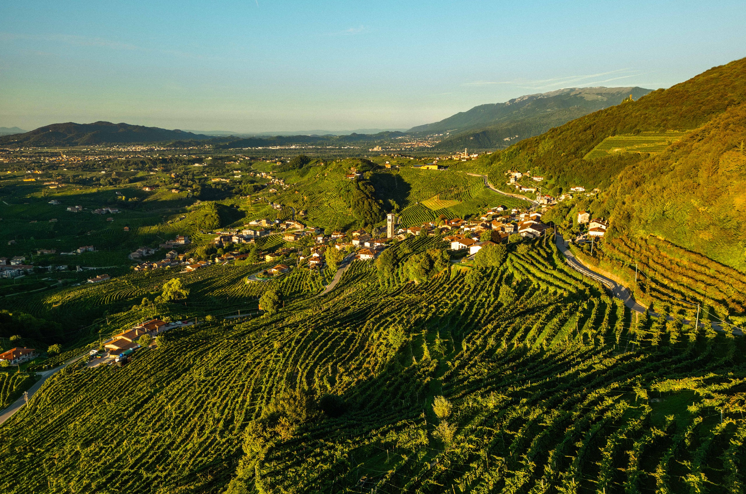Ariel shot of Cartizze hills, with vineyards and small villages, under a blue sky