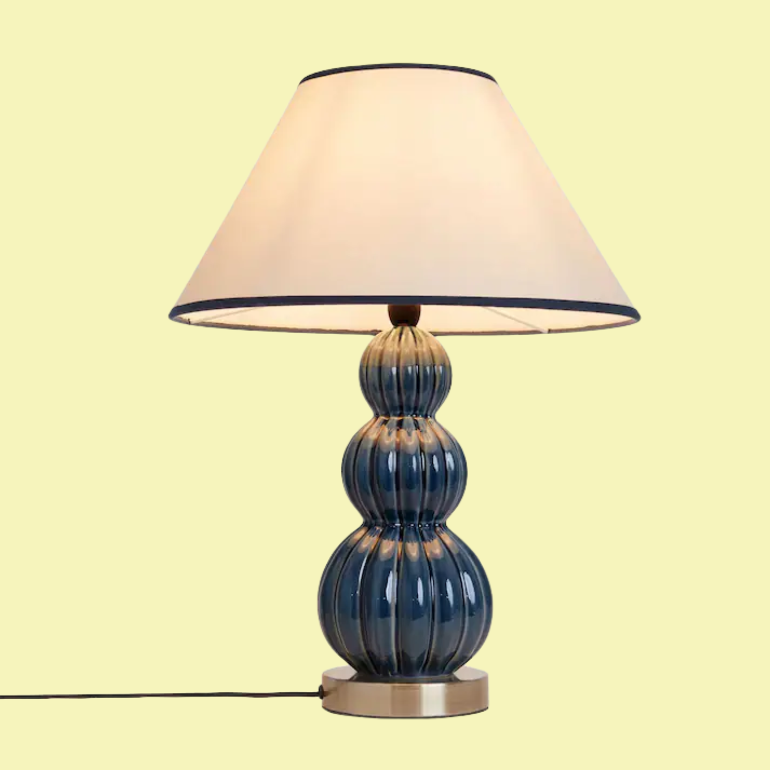A lamp with a brass foot, a curved and ribbed blue stem, and a white shade with a blue hem