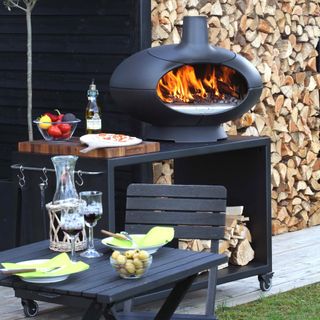 outdoor kitchen with black table top oven on unit with wheels, folding table and chairs, food, oil, pizza