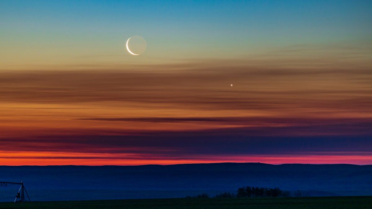 The conjunction of the waning crescent moon with Venus as they were rising low in the northeast dawn sky in southern Alberta, Canada. Earthshine is visible on the dark side of the moon. The sky exhibits the wonderful transition of colours from the orange at the horizon through the spectrum to the blues at top