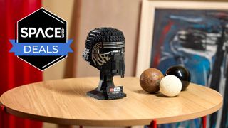 A black brick-built helmet with silver outlines around the eyes is on a display stand on a light brown wooden surface with the space.com logo in the top left corner.