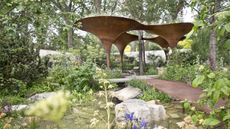 Water garden with large brown steel structure in centre and brown steel path over water