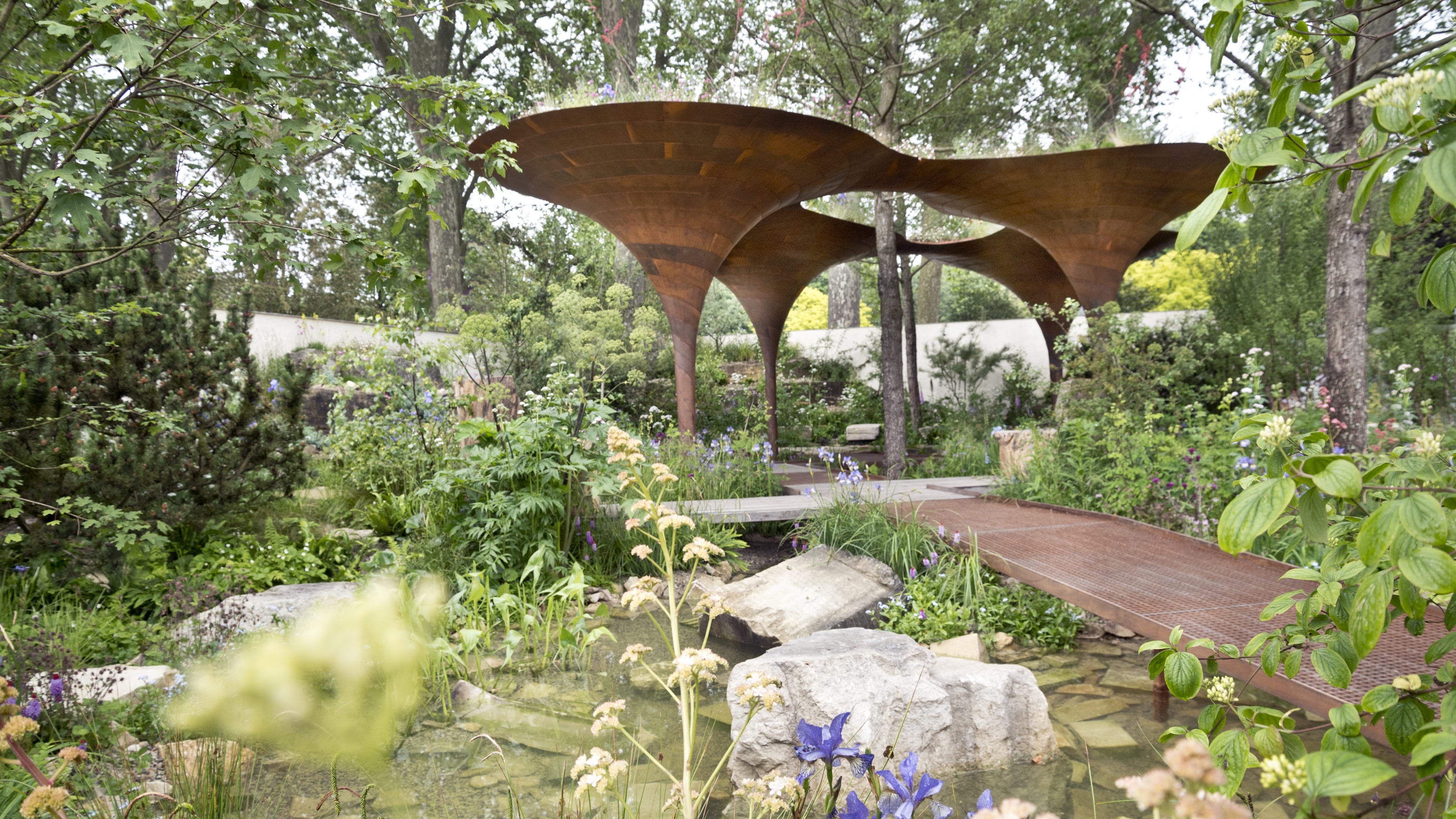 Water garden with large brown steel structure in centre and brown steel path over water