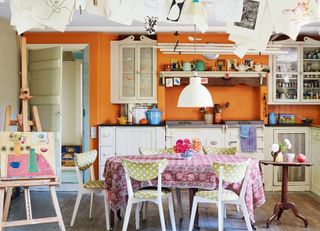 boho kitchen with orange walls pink table cloth and green and white spotted chairs