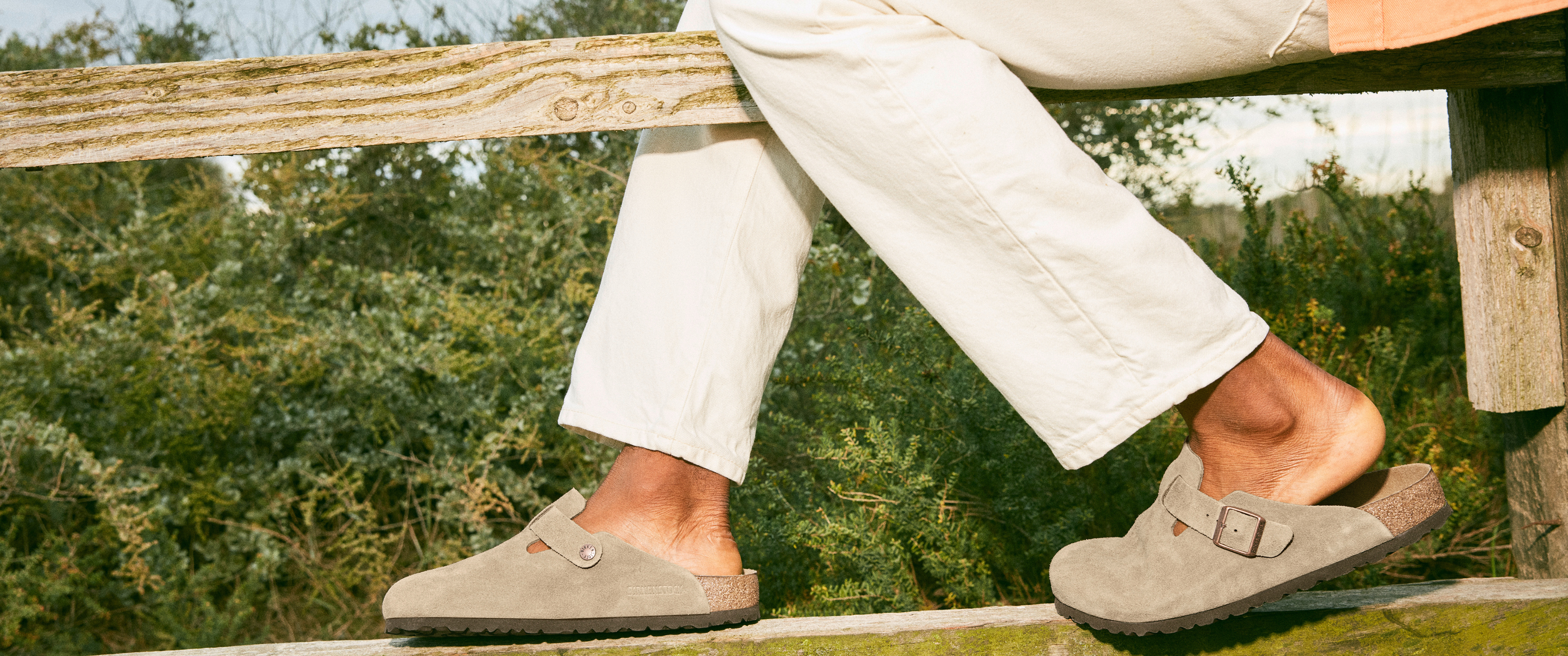 Model sat on a wooden fence wearing Birkenstock clogs sold at The Hut