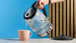 Cosori Electric Glass Kettle pouring water photographed in front of a blue background.