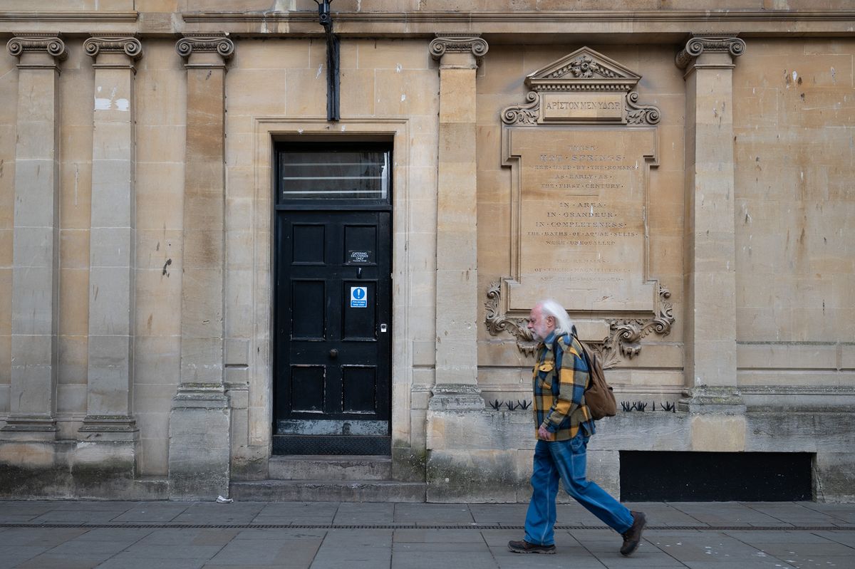 A man walks past a door and pillars on a historical building