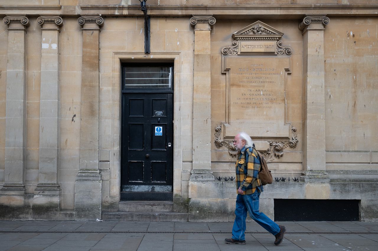 A man walks past a door and pillars on a historical building