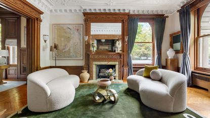 living room with wood paneling and ceiling moldings green rug and modern cream sofas 