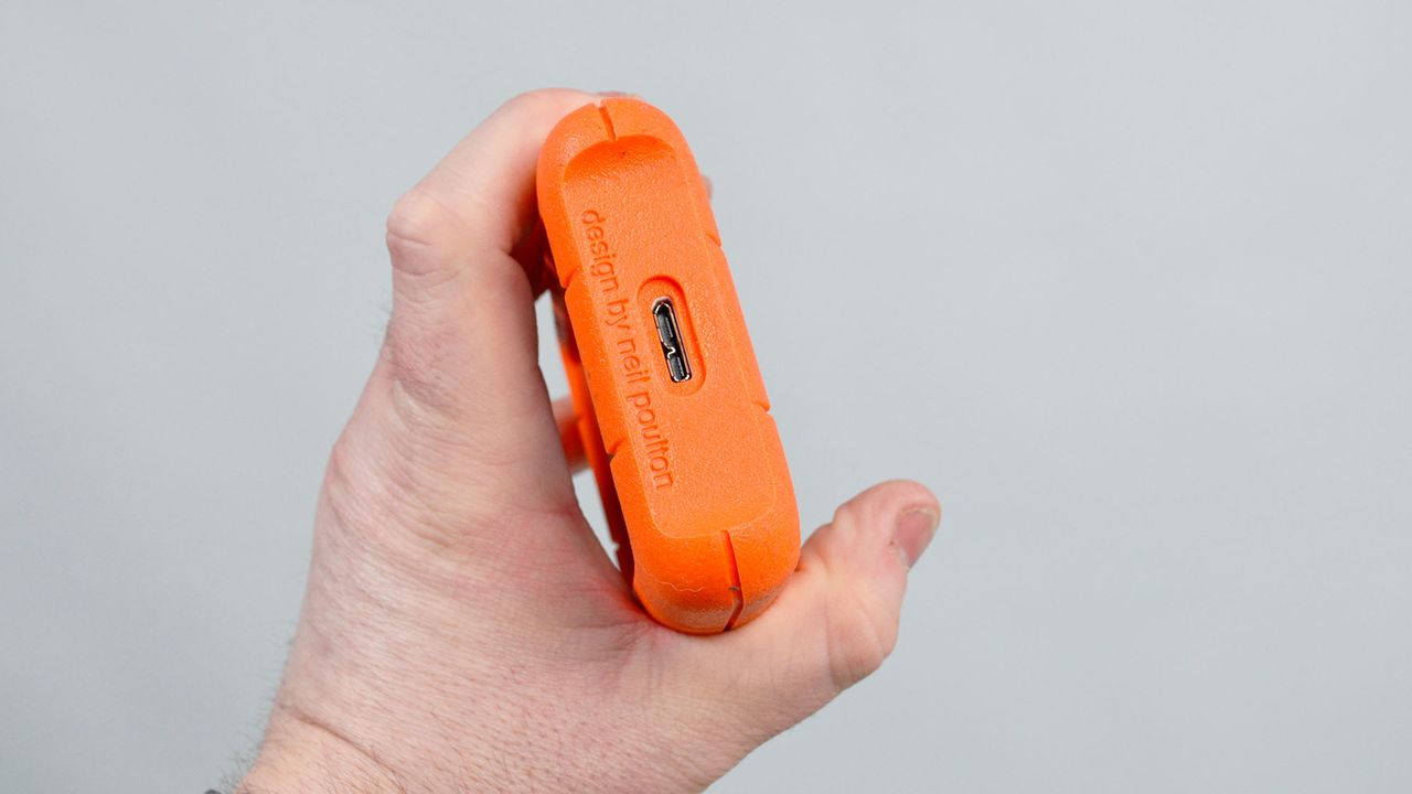 A masculine hand holding a LaCie Rugged Mini external hard drive