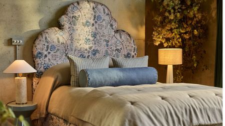 A cozy neutral bedroom with cream and blue floral headboard, mismatched but expensive looking bedside lamps, taupe bedding and blue throw pillows