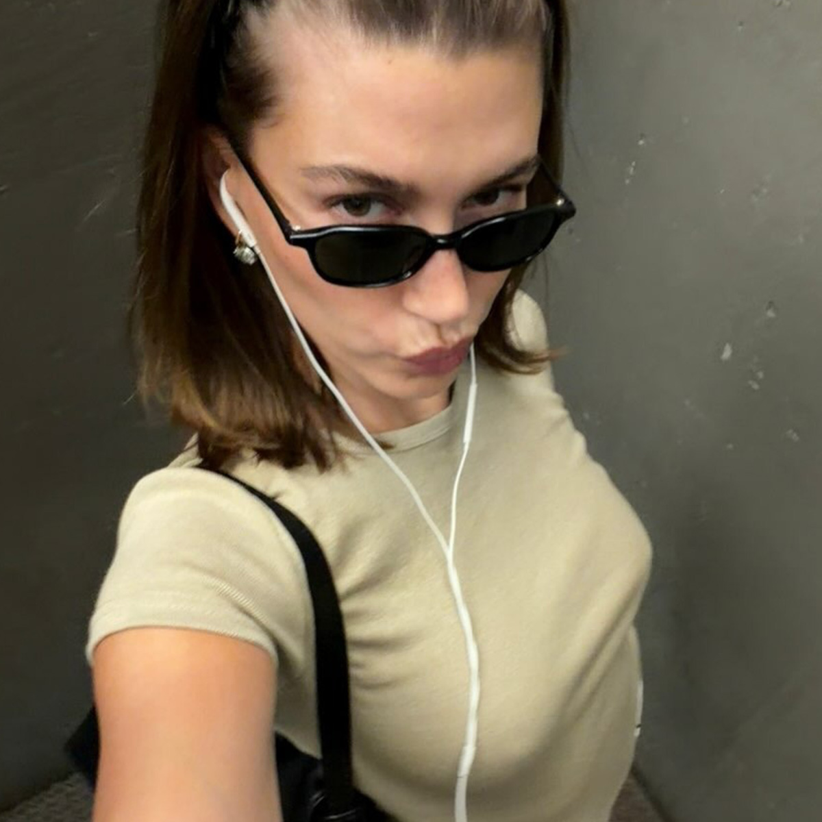 Hailey bieber wears a beige t-shirt and black sunglasses.