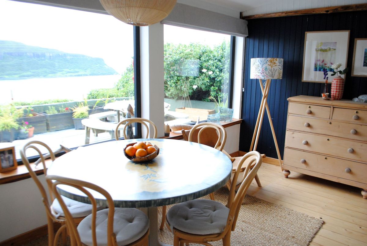 The dining room has a wooden table with four chairs and bifold windows looking out on views of a distant mountain and the gravelled garden