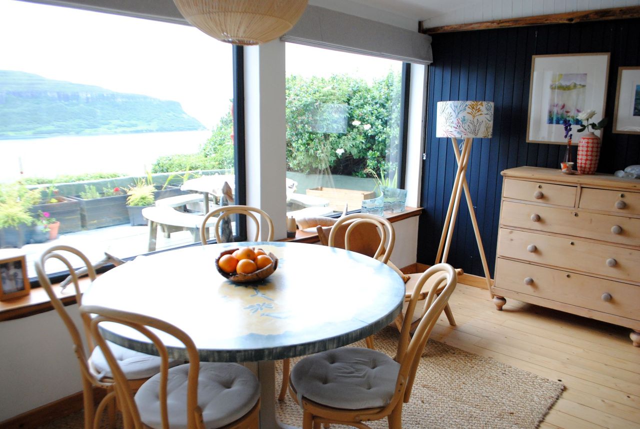 The dining room has a wooden table with four chairs and bifold windows looking out on views of a distant mountain and the gravelled garden