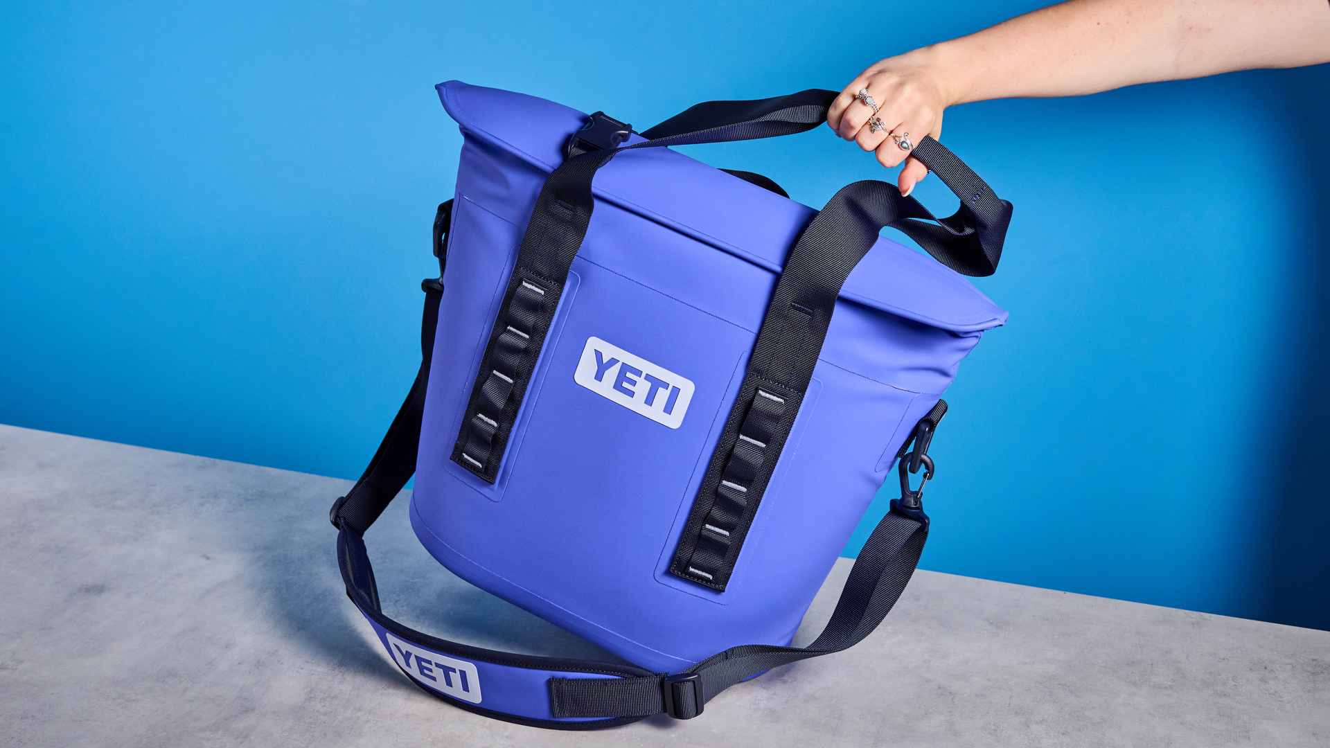 the yeti hopper m15 cool bag with a padded carry strap, handles, and a 15 quart capacity photographed with coke zero cans against a blue background