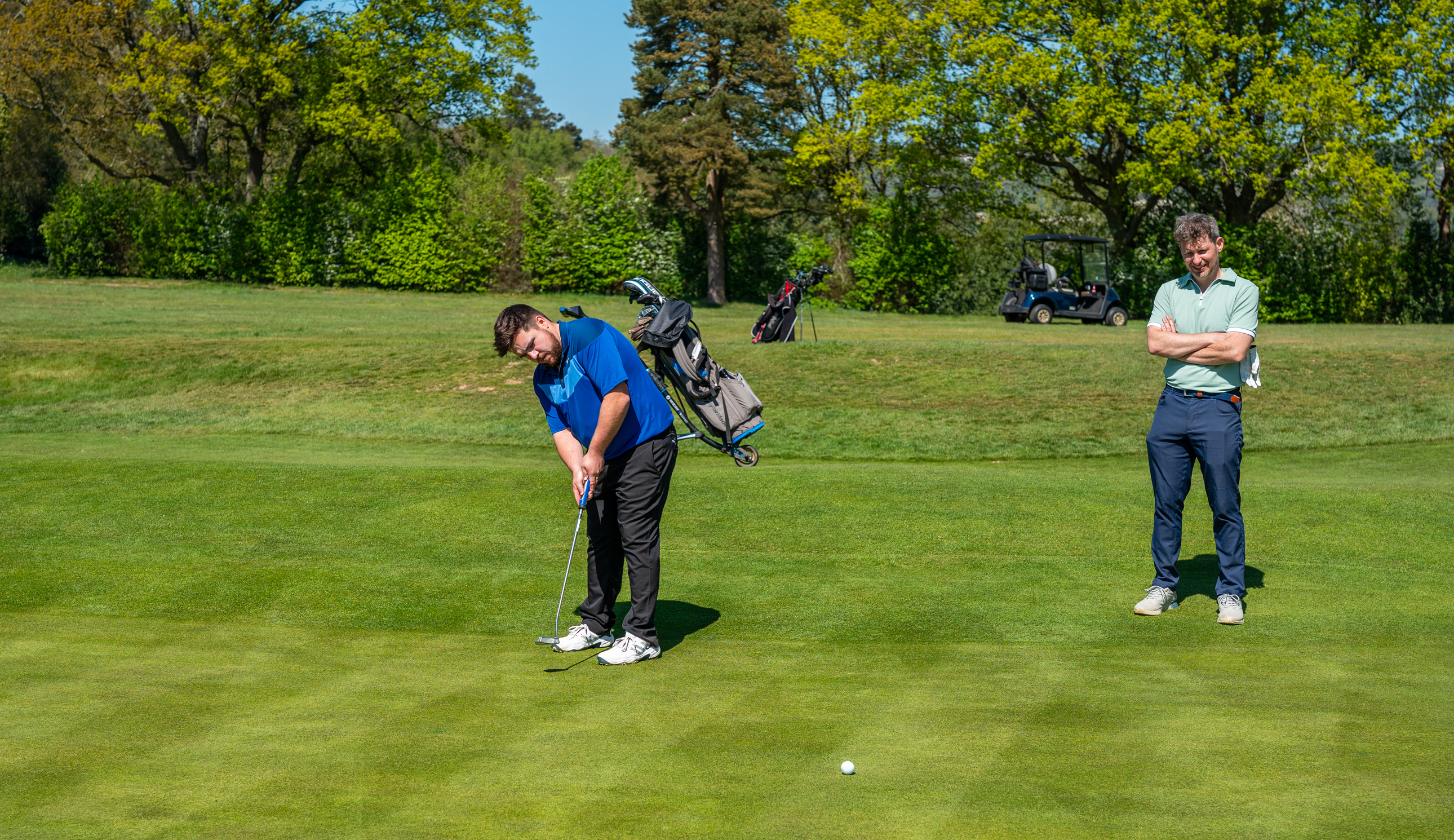 A golfer strikes a putt while another looks on