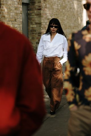 A woman in London wearing brown barrel pants and a white wrap blouse and black flats