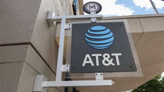 A black AT&T sign with its logo in bright blue hanging outside a brick store 