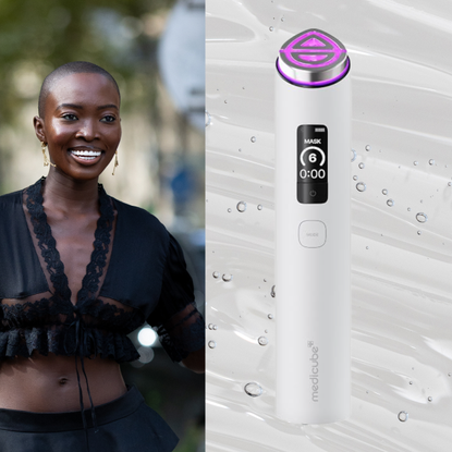 A woman smiling and wearing a black lace top. She is next to a beauty device, the medicube booster pro