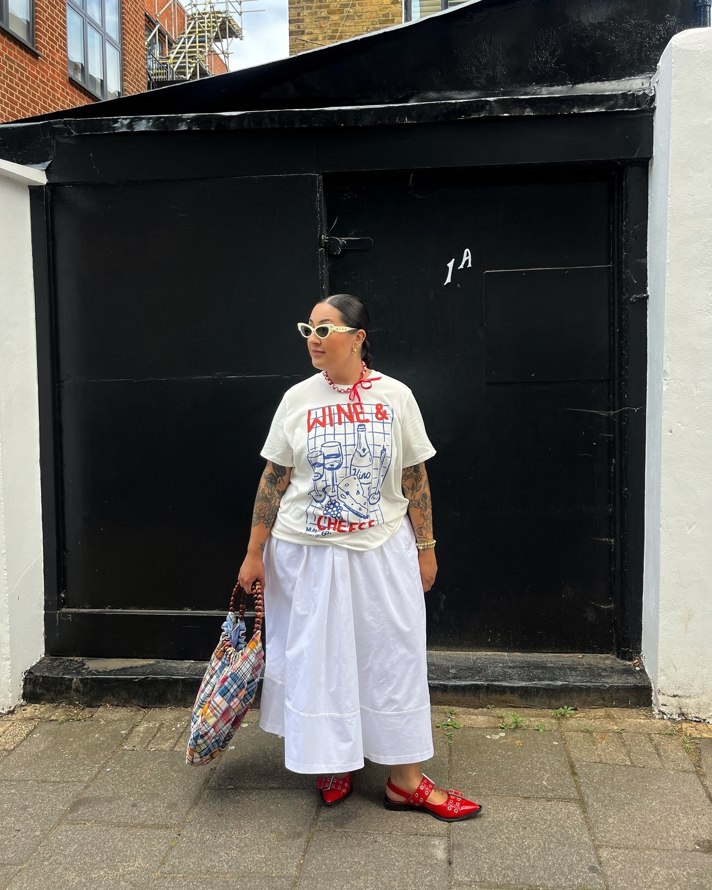 Mujer con camiseta estampada, falda midi blanca y sandalias rojas de Ganni.