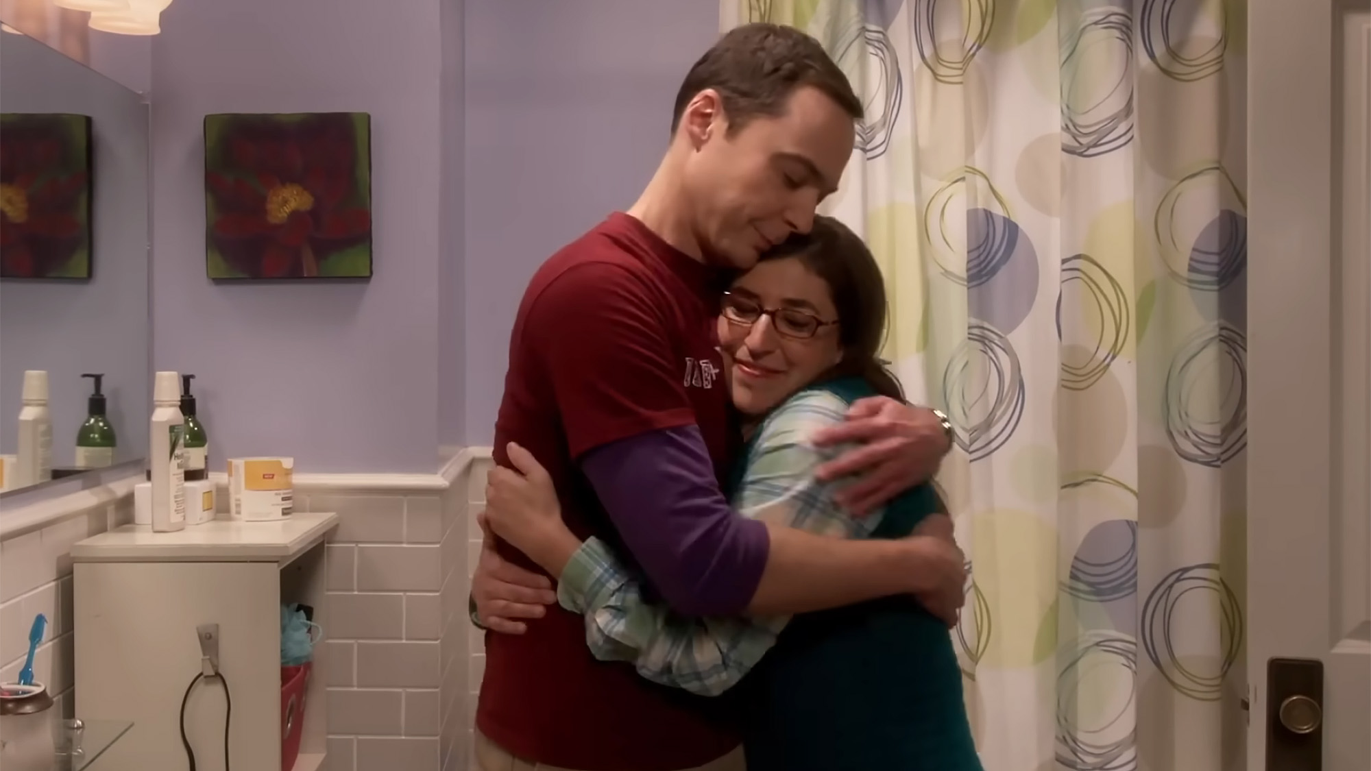 A screenshot of Sheldon and Amy hugging in their bathroom on the set of The Big Bang Theory. Both have on long-sleeved shirts. 