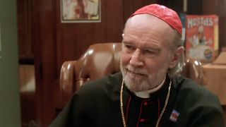 George Carlin wearing a priest outfit playing Father Glick in 1999's Dogma.