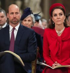 Prince William wearing a suit and a red tie sitting next to Kate Middleton wearing a red coat and hat at Commonwealth Day 2025