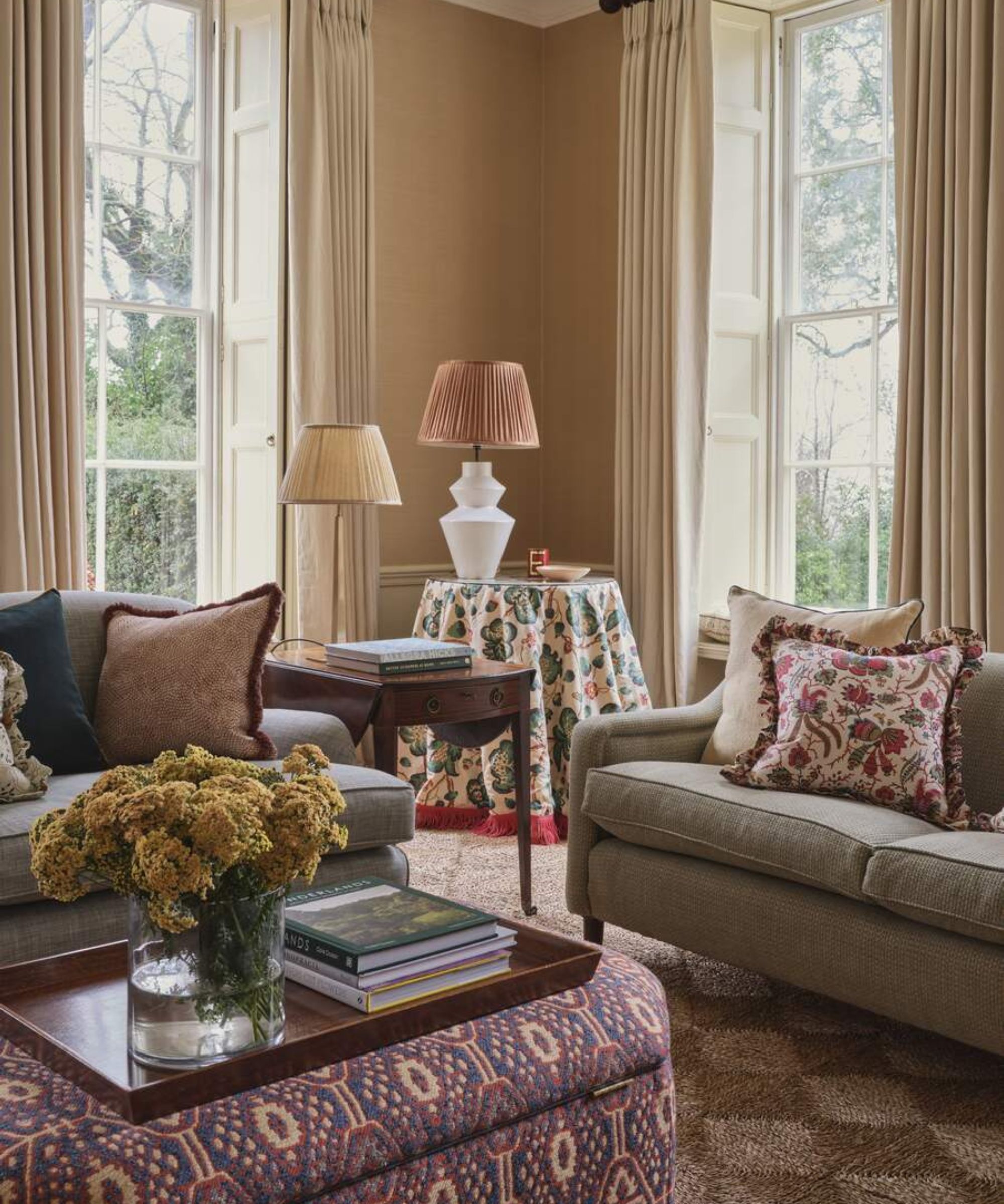 Pale peach toned living room with large windows, gray sofas and a patterned ottoman