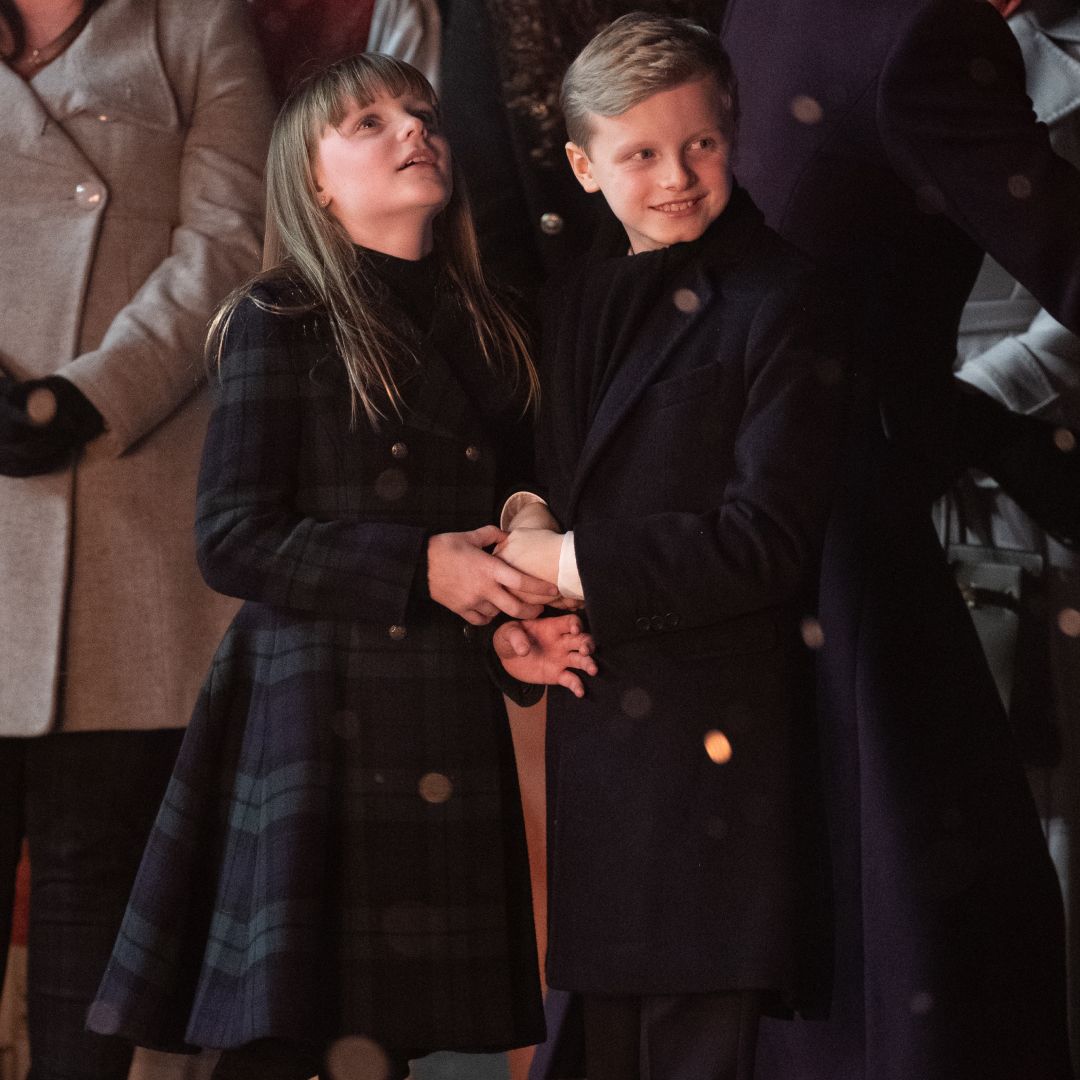 Princess Gabriella wearing a tartan blue and green coat holding hands with her brother Prince Jacques standing outside in front of a group of people