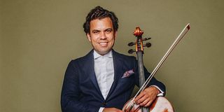 Musician Francesco Vila posing in a suit with his cello.