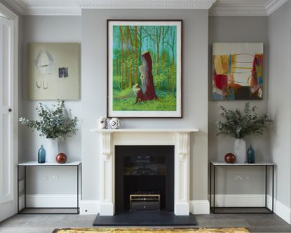 A pale gray living room with a white fireplace and three large artworks hung on the wall