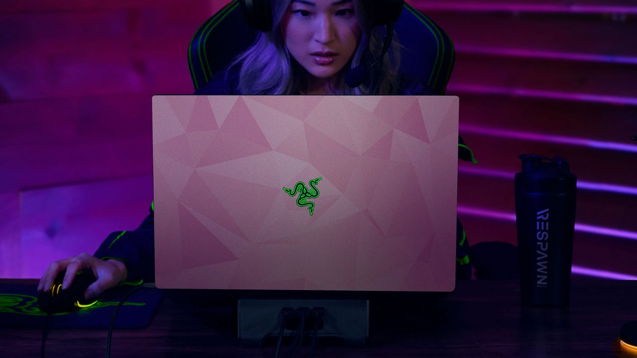 A young lady sits behind a Razer Blade laptop which has a Quartz Pink vinyl wrap from Razer.