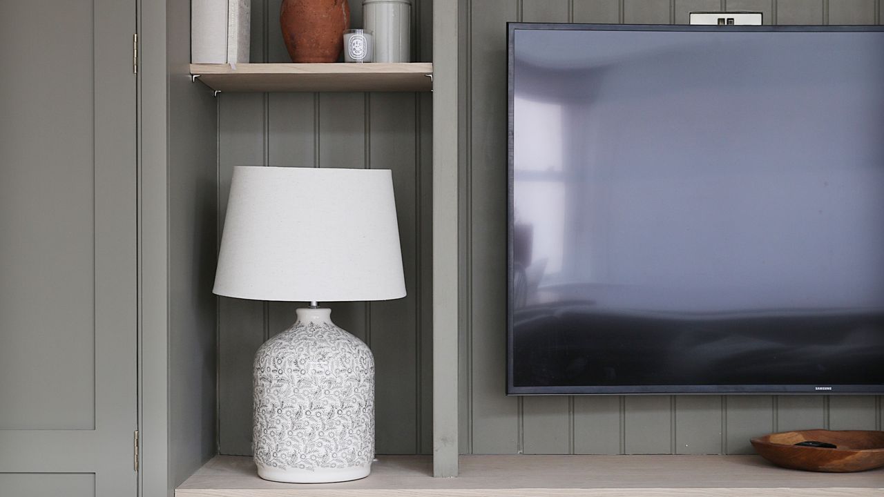 TV mounted on panelled media wall with shelving, decorated with table lamps, vases, and books