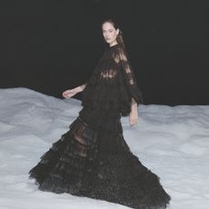 Model walking through snow wearing a black sheer tiered maxi dress sold at AllSaints